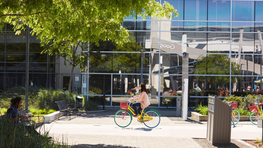 A  person riding a bike in front of a building with a mirror facade.