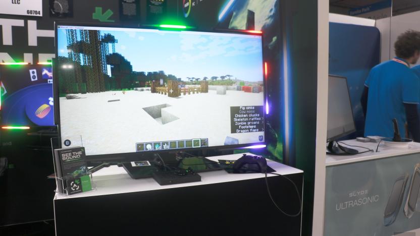 A monitor on a table, with the screen showing an environment in Minecraft. Surrounding the display are lights, with the middle top bar glowing in green, while those in the top right corner are showing red. The bottom corner is lit up in purple.