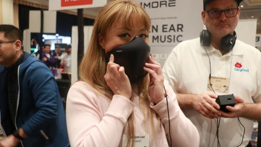 A person holding the Skyted mask to her face at a busy event with people and banners in the background.