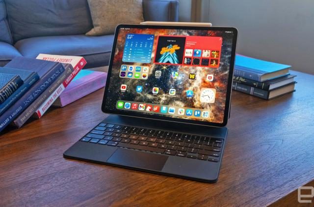 The Apple iPad Pro (2022) sitting upright on a coffee table with its keyboard out and the Pencil magnetically attached across the top.
