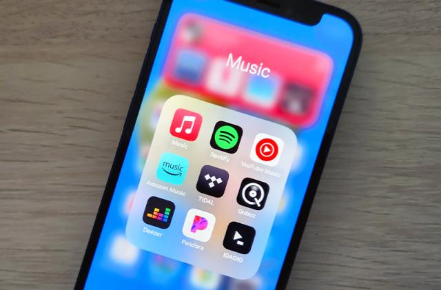 A smartphone lies on a desk, displaying icons for several music streaming apps.