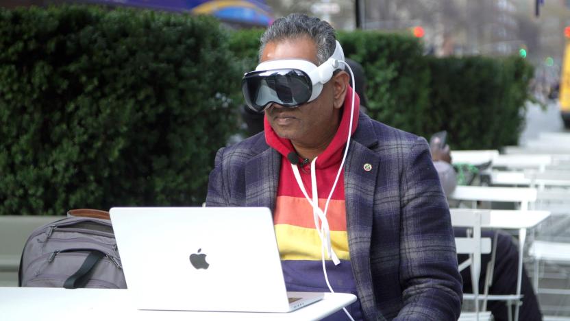 A person wearing a mixed reality headset sitting in front of a MacBook.