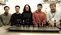 Group photo of five members of a research team focused on a scientific camera. They stand smiling in a laboratory with various imagine equipment on the research table in front of them.