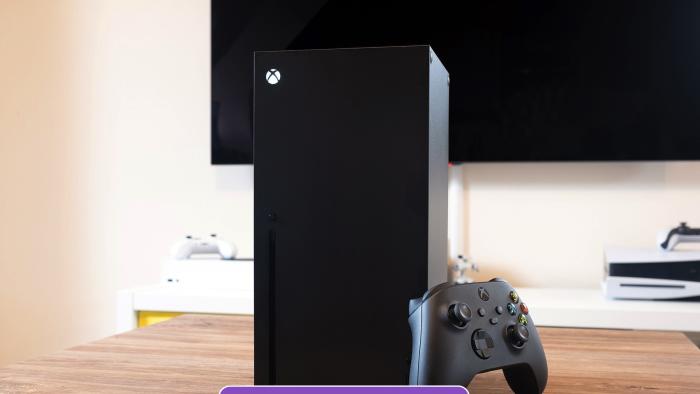 An Xbox Series X sits on a wooden coffee table with a PlayStation 5 and TV in the background.  