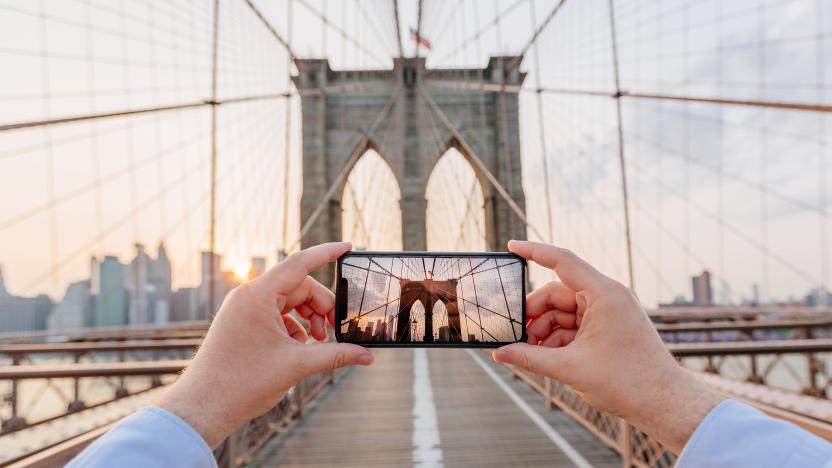 Personal perspective view of a man photographing Brooklyn Bridge using smartphone, New York, USA