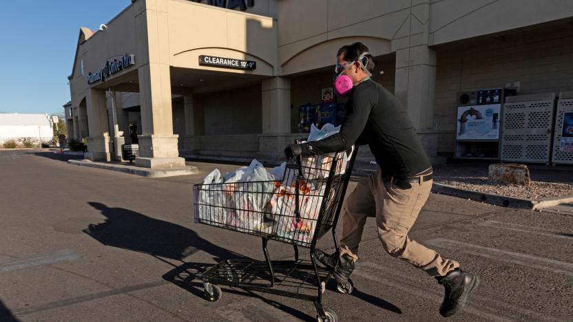 A person with a cart in the parking lot of a shopping center.