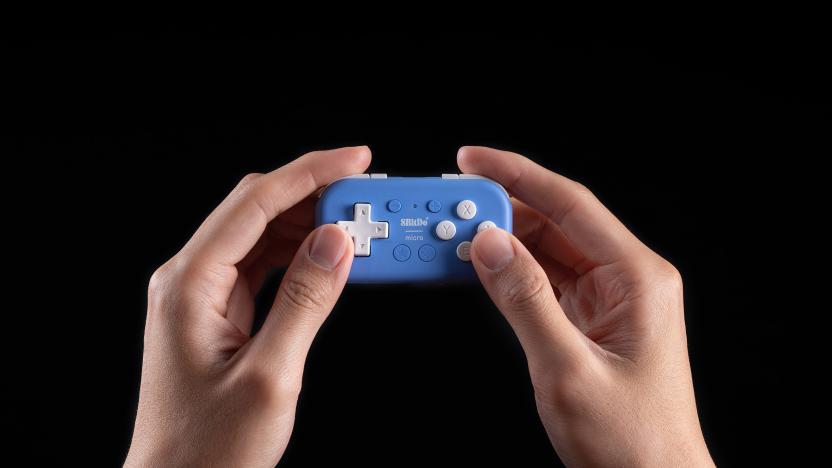 A pair of hands holding a tiny blue 8BitDo Micro gamepad in front of a black background.