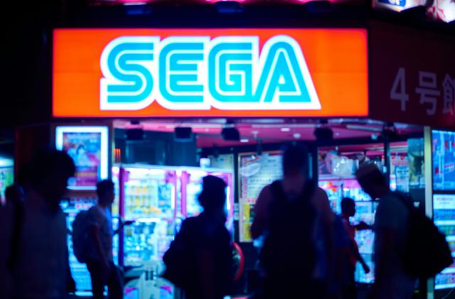 A group of people walk past a Sega sign.