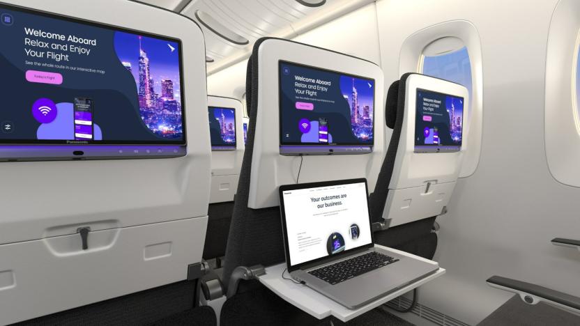 The backsides of plane seats in economy class installed with Panasonic Avionics' Astrova in-flight entertainment system screens. The screens display a notice that says "Welcome Aboard, relax and enjoy your stay." One tray is unfolded with an open laptop on top of it. 