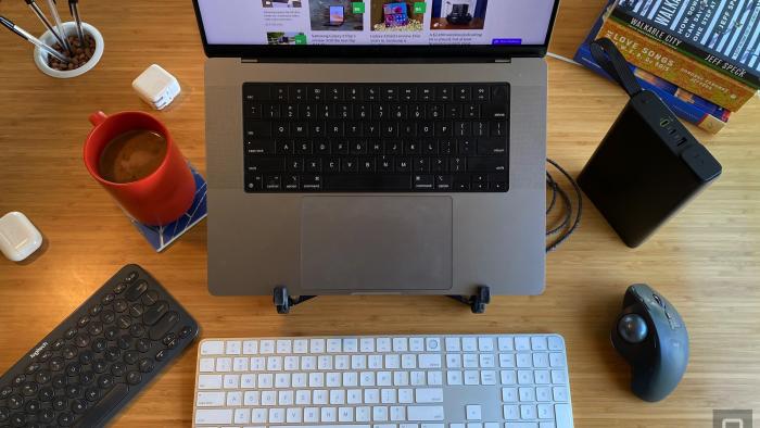 A MacBook Pro sits on a stand on a desk, surrounded by various keyboards and other useful accessories. 