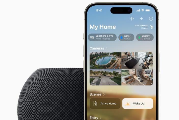 A HomePod mini in the color midnight (black) with an iPhone propped behind it. The image is cropped so only the top half of each device is show