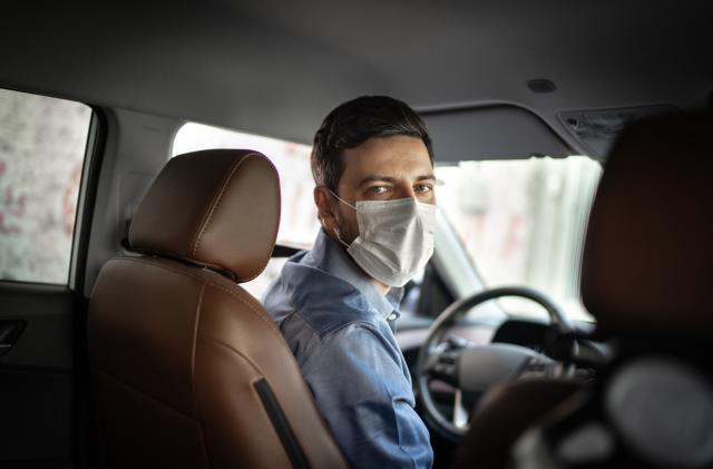 Driver taking to a passenger on seat back wearing protective medical mask