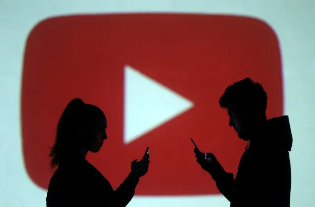 Silhouettes of mobile users are seen next to a screen projection of Youtube logo in this picture illustration taken March 28, 2018.  REUTERS/Dado Ruvic/Illustration