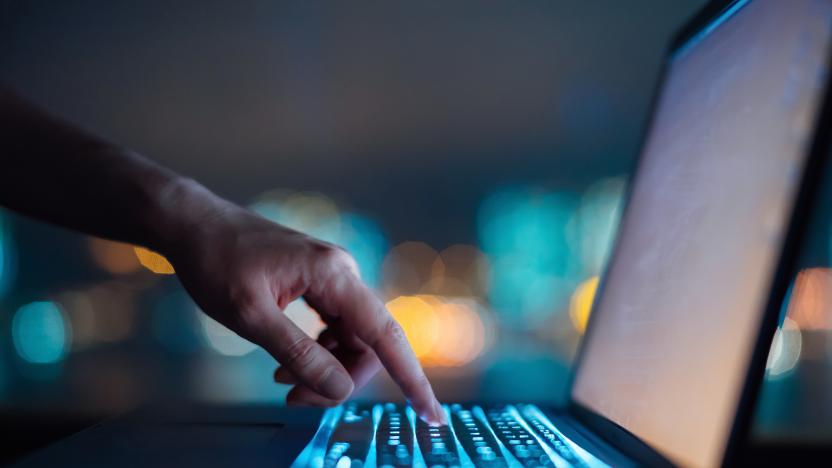 Close up of woman's hand typing on computer keyboard in the dark against colourful bokeh in background, working late on laptop at home