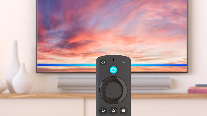 An image of a Fire TV stick standing in front of a TV. There are candles and tasteful vase. 