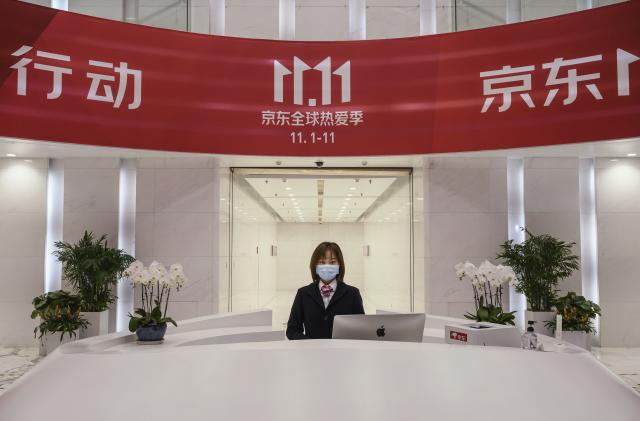 BEIJING, CHINA - NOVEMBER 11: A receptionist from Chinese e-commerce giant JD.com poses from her desk under the Singles Day banner in the lobby at the company's headquarters during an organized tour on November 11, 2020 in Beijing, China. The online shopping blitz, known as Singles Day or Double 11, is the world's largest retail event and comes as Chinese consumers are emerging from the COVID-19 pandemic. The revival of consumer consumption is expected to boost China's economy, which is already showing signs of post-pandemic recovery and providing a bright spot for global brands and retailers. Singles Day sales for China's biggest e-commerce giants like JD.com are on pace to break previous records, pulling in $56 billion U.S. in the first 30 minutes, when combined with three days of pre-event sales. (Photo by Kevin Frayer/Getty Images)