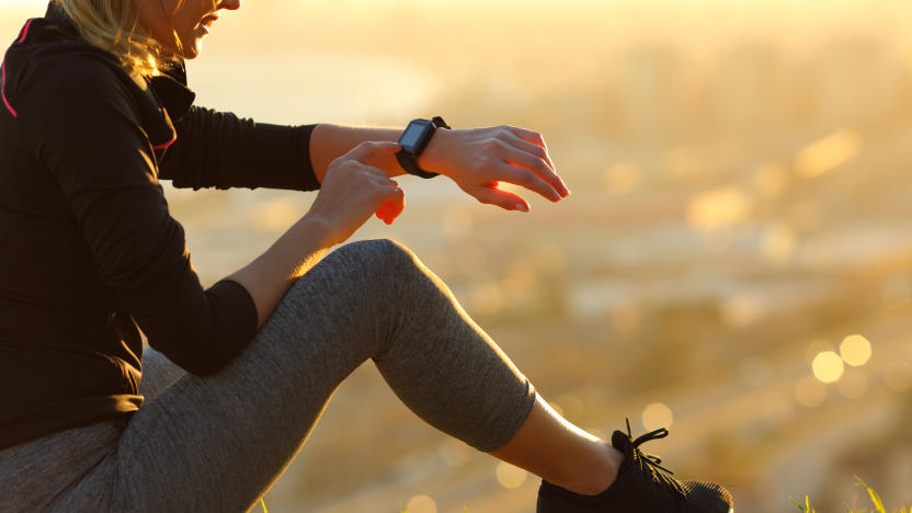 Runner sitting on the ground checking smartwatch after running at sunset