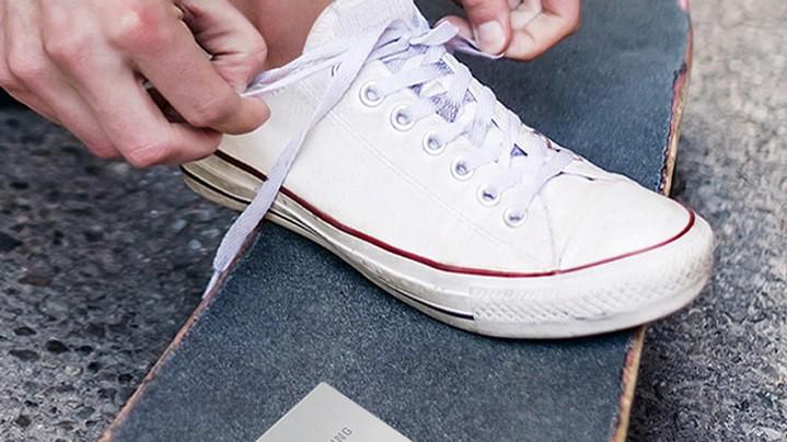 Samsung T7 touch portable hard drive placed on a skateboard, next to someone tying the laces of a sneaker.