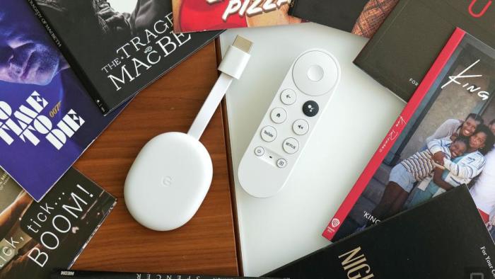 Review photo of the Chromecast with Google TV (HD). The streaming dongle and remote sit on a desk, surrounded by books.