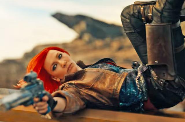 Cate Blanchett as Lilith in the movie Borderlands. In this action still, she lays on her back with legs in the air and aims a gun towards someone off camera.
