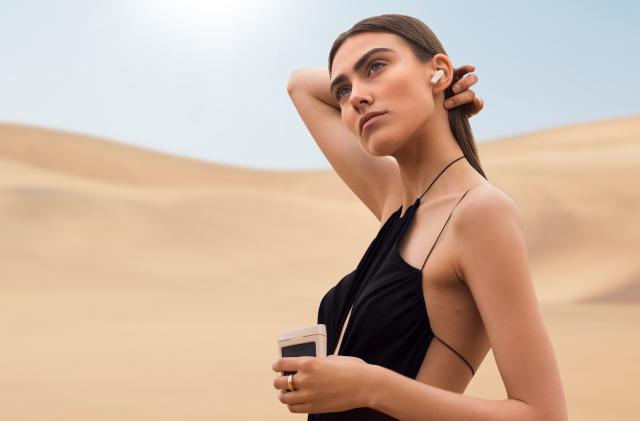 A model wearing an Urbanista Phoenix earbud and holding the charging case.