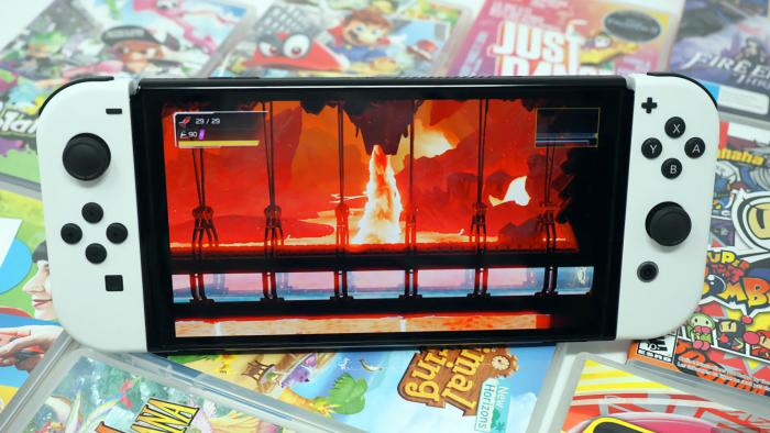 Photo of the Nintendo Switch OLED sitting on a colorful array of game cartridge cases. Its screen shows a fiery scene.