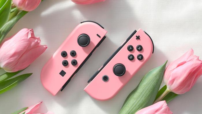 Marketing image for peach pastel-colored Joy-Con controllers for the Nintendo Switch. The two halves lie on a white tablecloth next to pink roses.