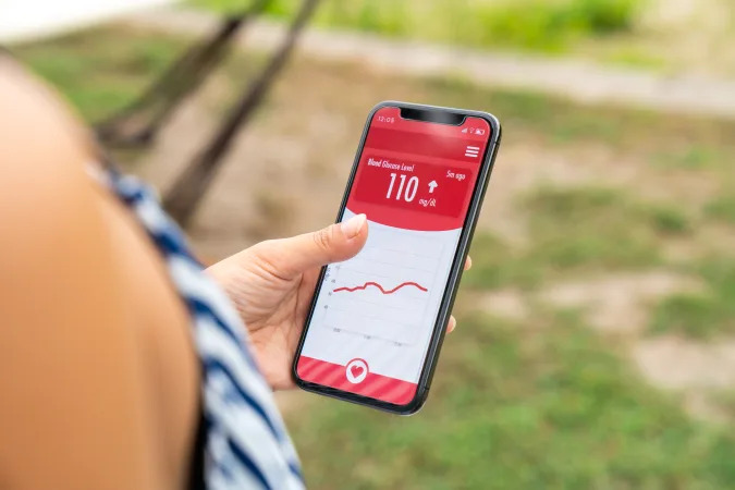 Woman wearing a glucose sensor checking her blood sugar level using a smartphone app. Tottori, Japan