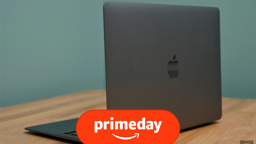 A silver MacBook Air laptop sits on a brown desk in front of a blue wall, with its back facing the camera at an angle, showcasing an Apple logo.