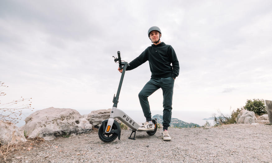 Image of F1 driver Lando Norris stood beside a Pure Electric Advance e-scooter.