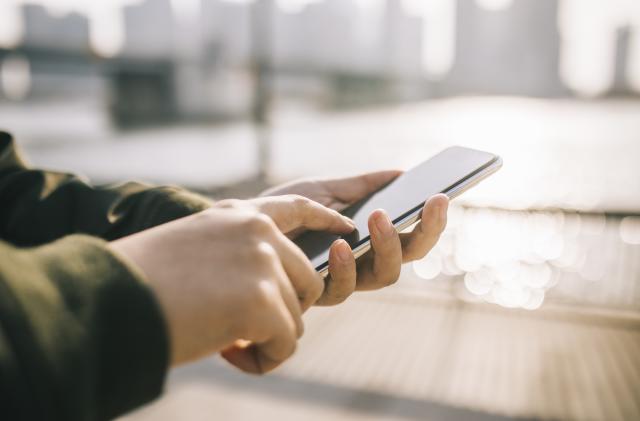 Close up of man's hand using smartphone on the go in the city against sunlight.