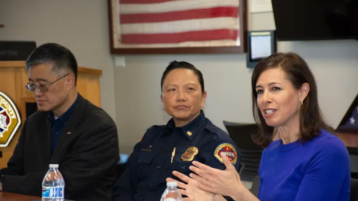 A man in black, a cop and a woman wearing a blue top sitting together.