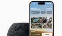 A HomePod mini in the color midnight (black) with an iPhone propped behind it. The image is cropped so only the top half of each device is show