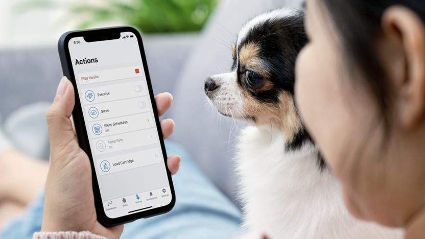 A person holding a phone showing the interface of a diabetes care app, with a dog next to them.