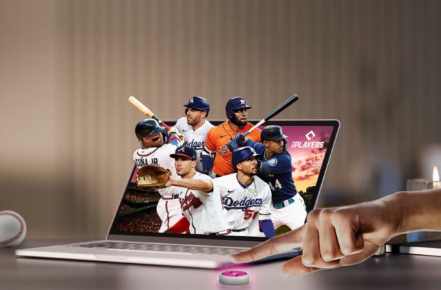 Promotional image for T-Mobile and Major League Baseball’s annual subscription deal for fans. Six MLB players are popping out of a laptop screen as a hand reaches into the frame to press a pink button on the desk in front of the laptop.