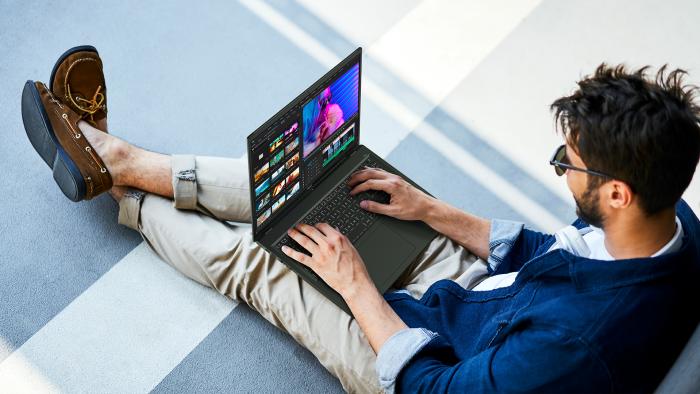 Top-down view of a person sitting outdoors on a curb, using the Acer Swift Edge 16 laptop.