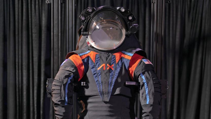 The Axiom Space AxEMU spacesuit for Artemis III Moon mission is presented against a black curtain. The suit is helmeted and mostly dark grey with blue and orange accents.