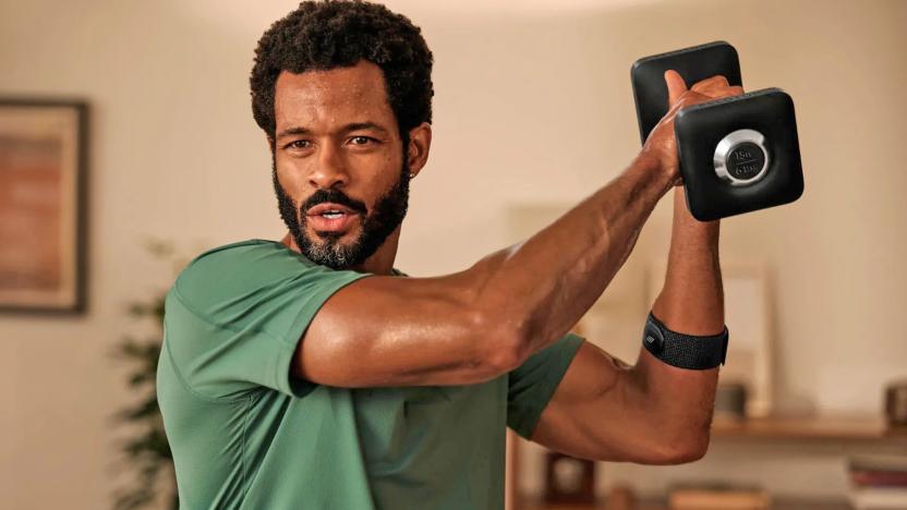 A man holds up a dumb bell during a workout in his living room.