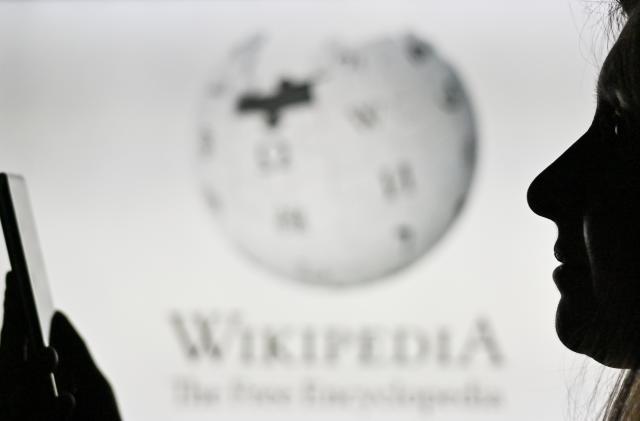 An image of a woman holding a cell phone in front of the Wikipedia logo displayed on a computer screen.
On Tuesday, January 12, 2021, in Edmonton, Alberta, Canada. (Photo by Artur Widak/NurPhoto via Getty Images)