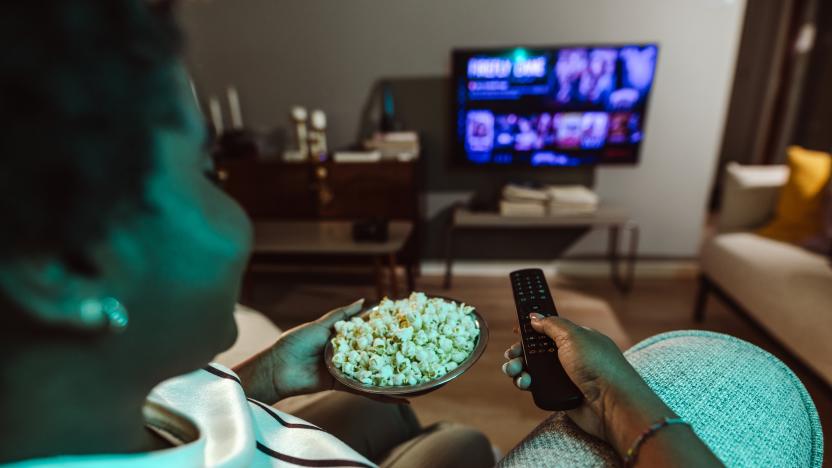 Cheerful smiling woman is watching TV and holding the remote control. Cozy night at home