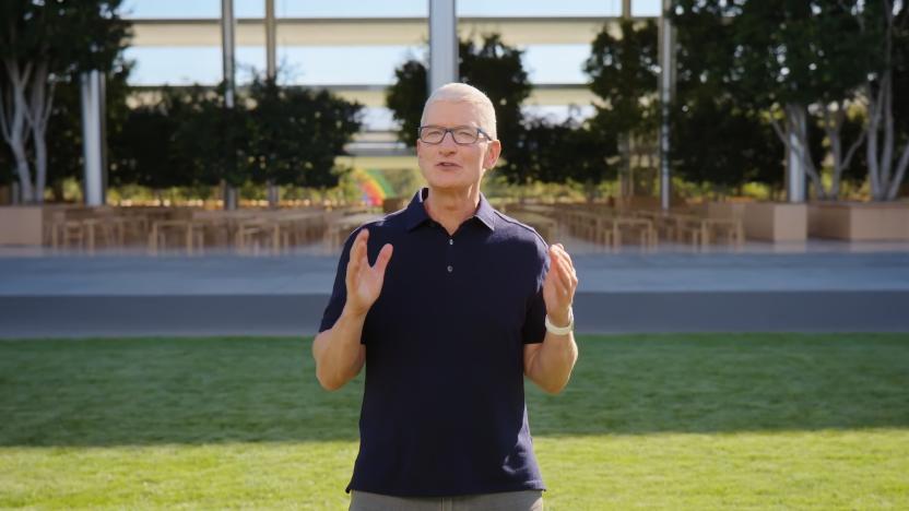 Screenshot of Tim Cook presenting at Apple's September 2022 iPhone launch event. He stands outdoors at Apple Park, on green grass in front of the "spaceship" building, holding two hands in front of him to emphasize a point.