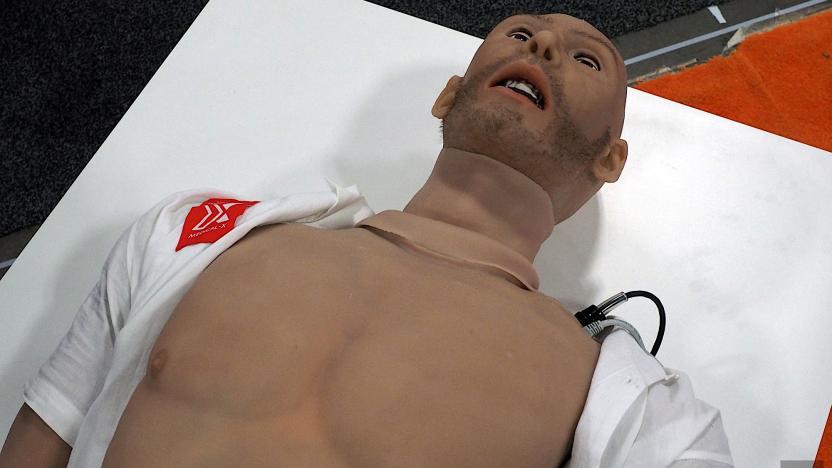 Image of the Adam-X medical training robot, an artificial human body laying on a white dais with the shirt open.