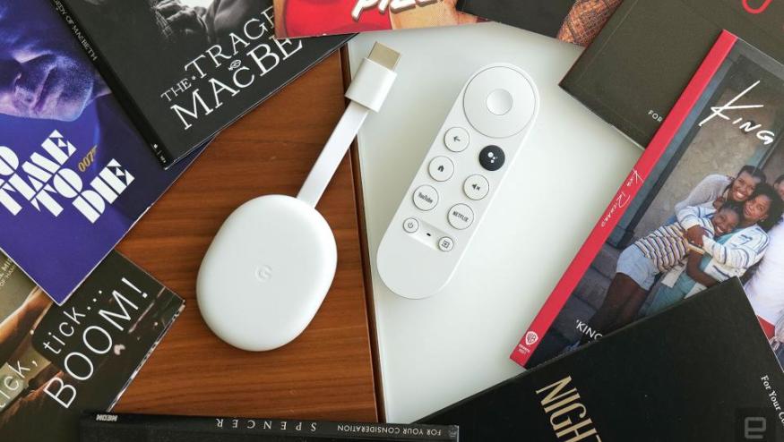 Review photo of the Chromecast with Google TV (HD). The streaming dongle and remote sit on a desk, surrounded by books.