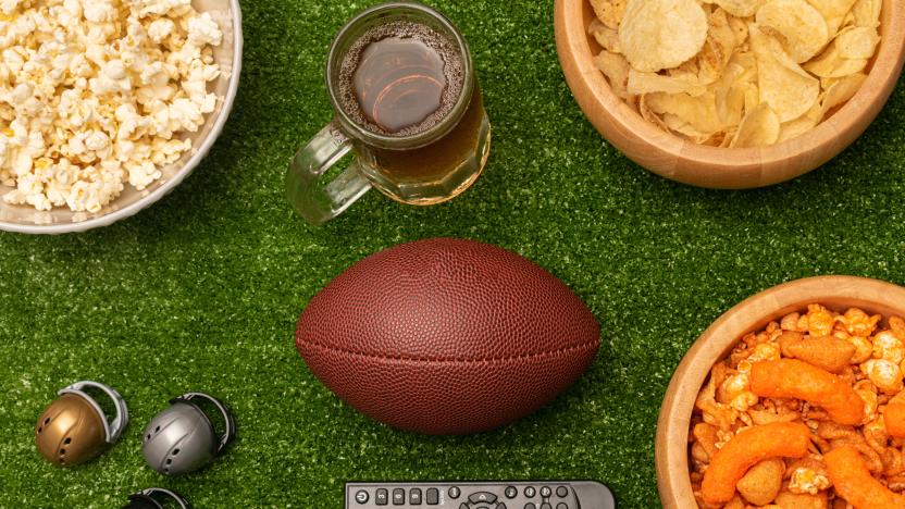 Super bowl flat lay photography with snacks, beer, american football ball, little helmets and remote control on green grass background