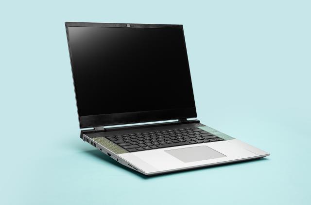 Product marketing photo of the Framework Laptop 16 modular notebook. The gray laptop (screen off) faces the 4:00 position in front of an aqua / teal background.