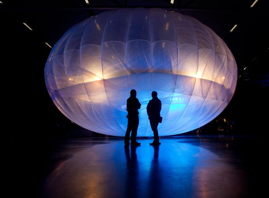 Visitors stand next to a high altitude WiFi internet hub, a Google Project Loon balloon, on display at the Airforce Museum in Christchurch on June 16, 2013. Google revealed top-secret plans on June 15 to send balloons to the edge of space with the lofty aim of bringing Internet to the two-thirds of the global population currently without web access.     AFP PHOTO / MARTY MELVILLE        (Photo credit should read Marty Melville/AFP via Getty Images)