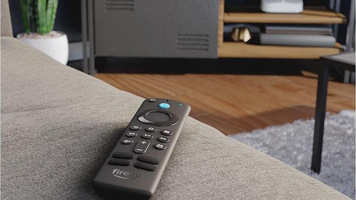 The remote for Amazon's Fire TV stick sits on a couch, pointed towards an entertainment center. 