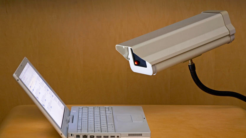 A surveillance camera is peering into the screen of a laptop computer.
