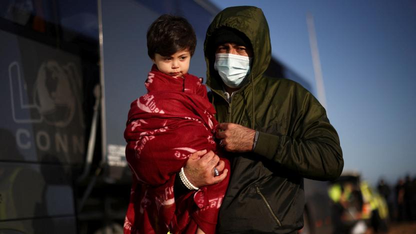 A migrant carries his child along the beach, as a group of migrants are processed by immigration officers, after crossing the English Channel in an inflatable dinghy, in Dungeness, Britain, January 18, 2022. REUTERS/Henry Nicholls