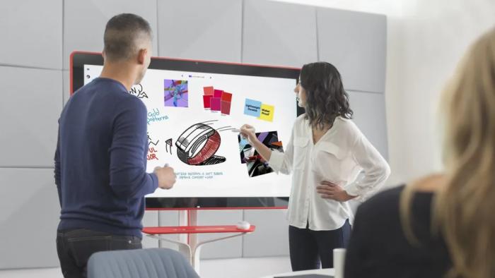 Two people standing in front of a digital whiteboard.